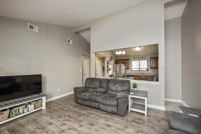 living room featuring high vaulted ceiling, sink, a chandelier, a textured ceiling, and light hardwood / wood-style flooring