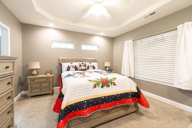 carpeted bedroom featuring ceiling fan and a tray ceiling