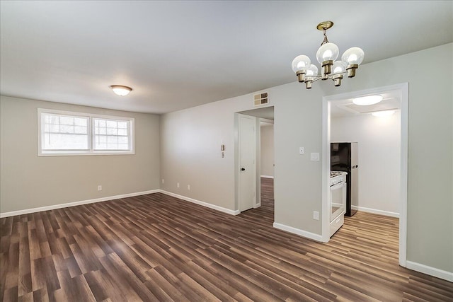 spare room featuring dark wood-type flooring and an inviting chandelier