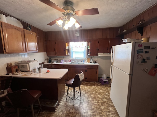 kitchen featuring sink, a kitchen breakfast bar, a textured ceiling, kitchen peninsula, and white fridge