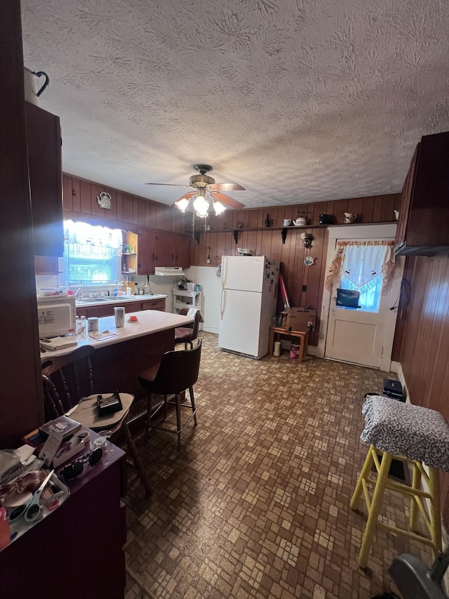 dining room with ceiling fan, a textured ceiling, and wooden walls