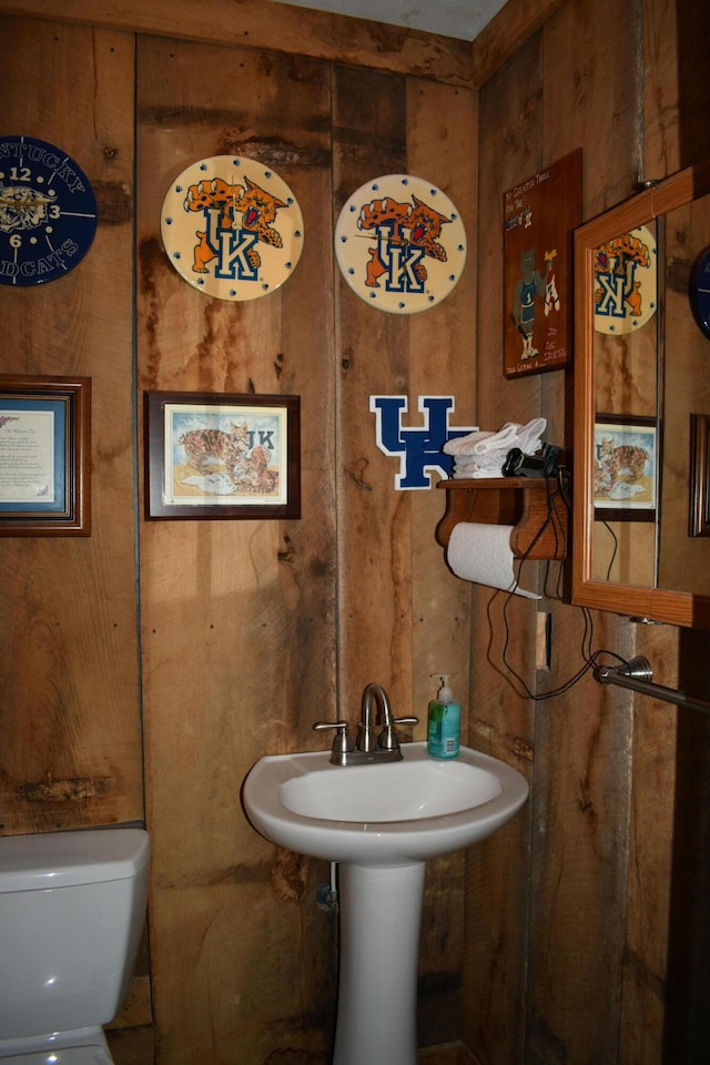 bathroom with sink, wooden walls, and toilet