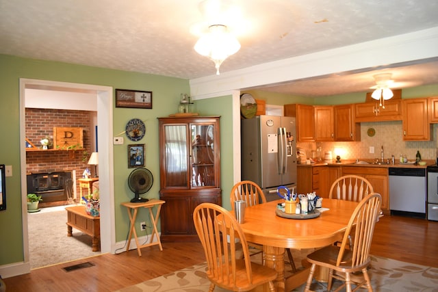 dining area featuring hardwood / wood-style floors, sink, a textured ceiling, and a brick fireplace