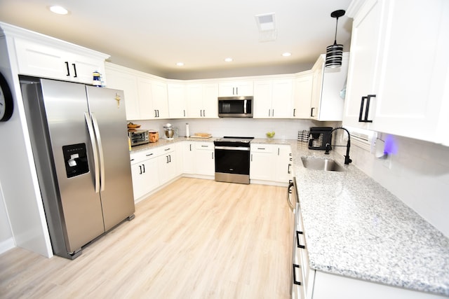 kitchen featuring hanging light fixtures, stainless steel appliances, sink, and white cabinets