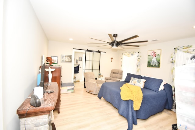 bedroom with ceiling fan, a barn door, and light wood-type flooring