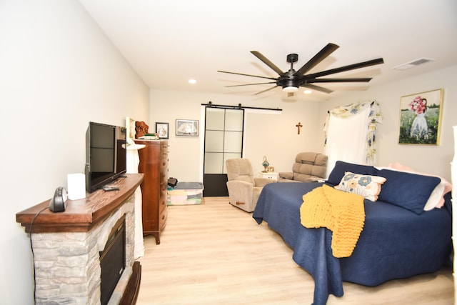 bedroom featuring a fireplace, a barn door, ceiling fan, and light wood-type flooring