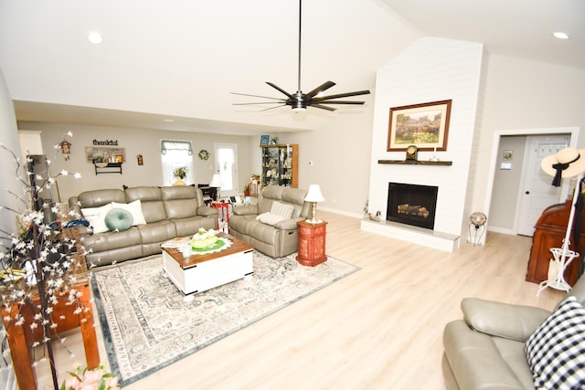 living room featuring vaulted ceiling, ceiling fan, a fireplace, and light hardwood / wood-style floors