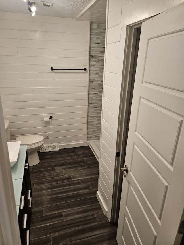 bathroom featuring wood walls, hardwood / wood-style flooring, vanity, toilet, and a textured ceiling