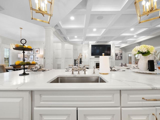 kitchen featuring coffered ceiling, sink, light stone counters, pendant lighting, and decorative columns