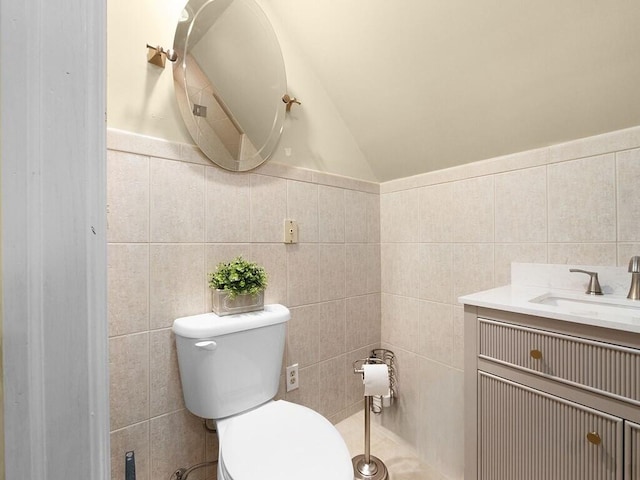 bathroom with lofted ceiling, vanity, toilet, and tile walls