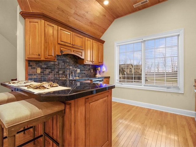 kitchen with sink, a breakfast bar area, backsplash, light hardwood / wood-style floors, and vaulted ceiling