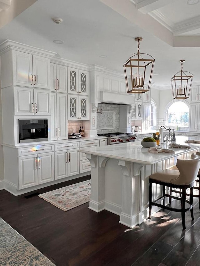 kitchen with dark wood-type flooring, a kitchen bar, white cabinetry, ornamental molding, and pendant lighting