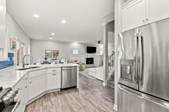 kitchen with sink, stainless steel appliances, ornamental molding, white cabinets, and light wood-type flooring