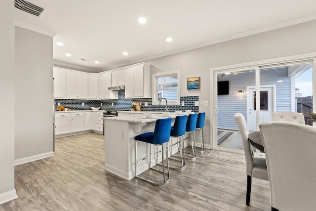 kitchen with backsplash, light stone countertops, white cabinets, a kitchen bar, and kitchen peninsula