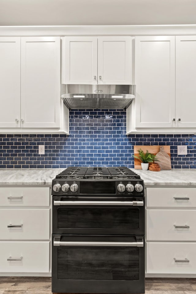 kitchen with range hood, white cabinets, and range with two ovens