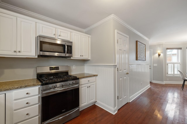 kitchen with appliances with stainless steel finishes, dark stone countertops, ornamental molding, white cabinets, and dark hardwood / wood-style flooring