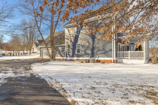 view of snowy exterior featuring a garage, central AC unit, and covered porch