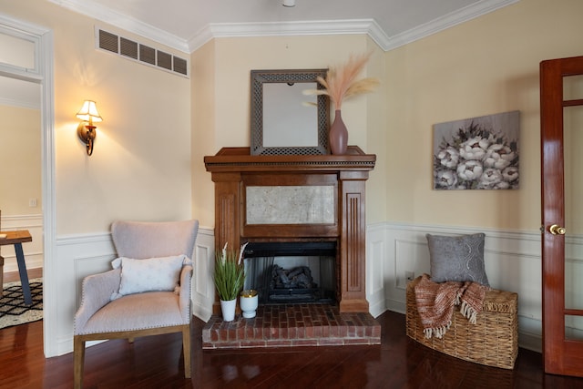 living area with crown molding, a brick fireplace, and hardwood / wood-style floors