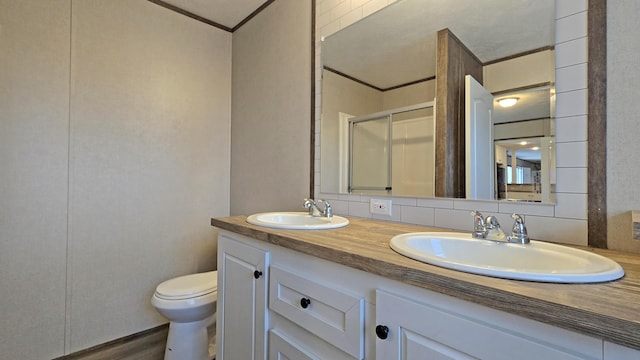 bathroom featuring toilet, a shower with shower door, ornamental molding, vanity, and decorative backsplash