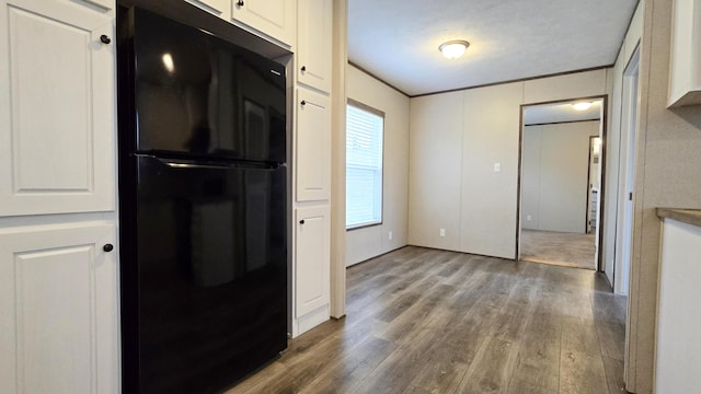 kitchen featuring wood-type flooring, ornamental molding, white cabinets, and black fridge