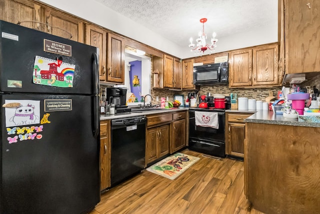 kitchen featuring sink, an inviting chandelier, black appliances, light wood-type flooring, and backsplash