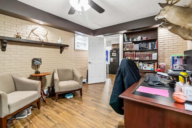 office area with ceiling fan, brick wall, and light hardwood / wood-style floors