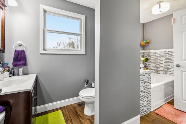 bathroom with tasteful backsplash, a tub to relax in, hardwood / wood-style flooring, vanity, and toilet