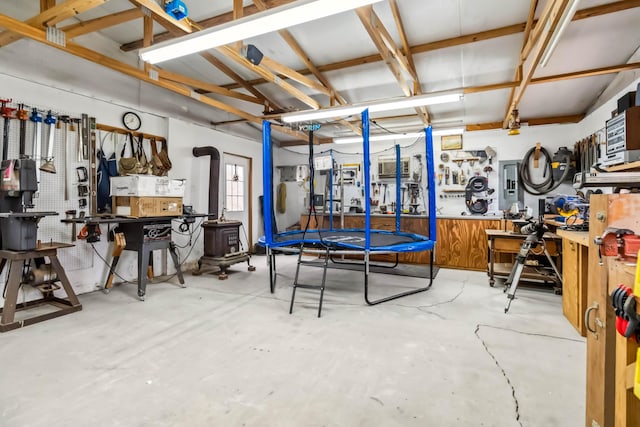 garage featuring electric panel, a wood stove, a trampoline, and a workshop area