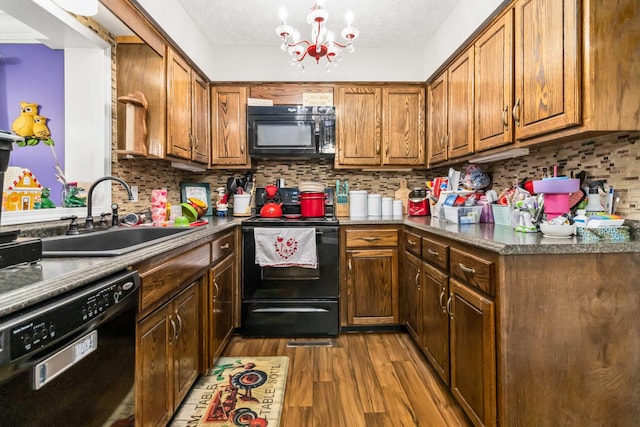 kitchen with sink, backsplash, black appliances, an inviting chandelier, and light hardwood / wood-style flooring