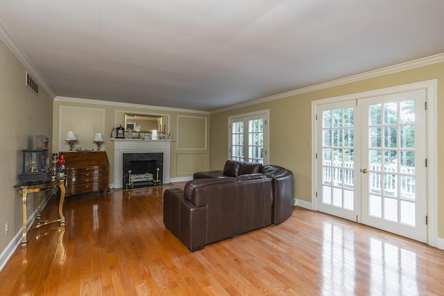 living room featuring french doors, a high end fireplace, crown molding, and light hardwood / wood-style floors