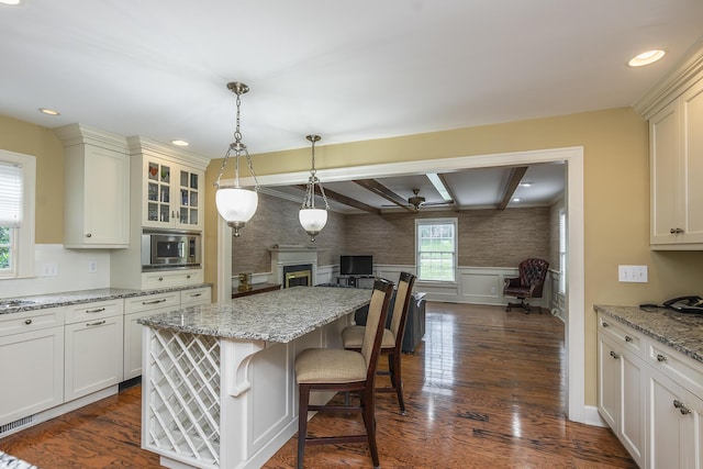 kitchen featuring light stone counters, stainless steel microwave, dark wood-type flooring, and a breakfast bar area