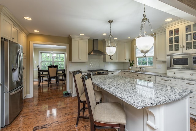 kitchen with pendant lighting, wall chimney range hood, a breakfast bar, appliances with stainless steel finishes, and a kitchen island