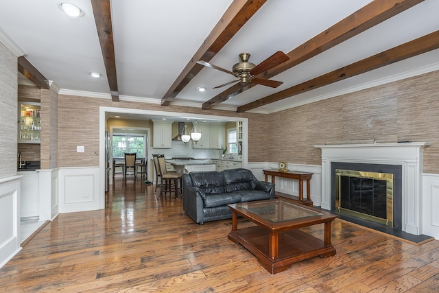 living room with hardwood / wood-style flooring, ceiling fan, ornamental molding, and beam ceiling