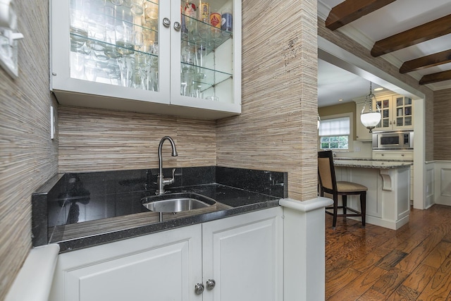 interior space with sink, dark stone countertops, stainless steel microwave, white cabinets, and decorative light fixtures