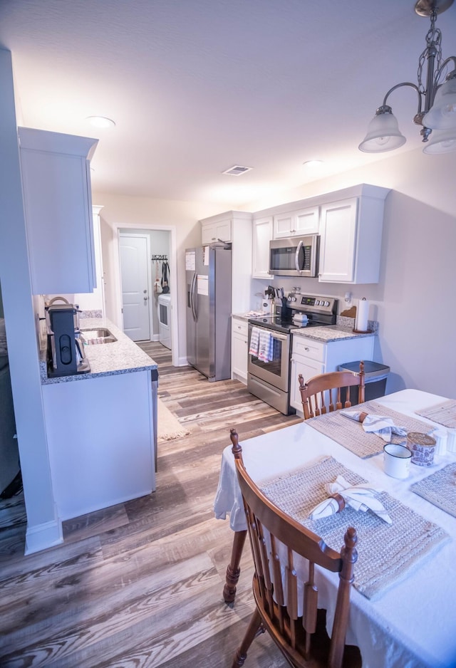 kitchen featuring light hardwood / wood-style flooring, appliances with stainless steel finishes, white cabinetry, hanging light fixtures, and light stone countertops