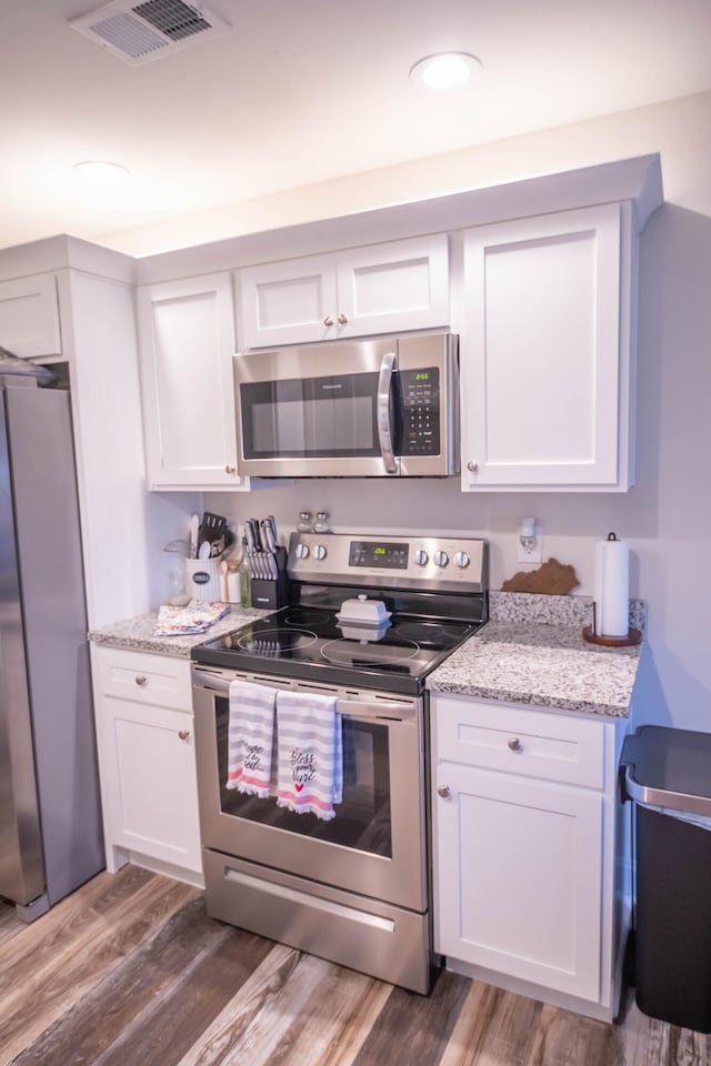 kitchen with stainless steel appliances, light stone countertops, dark wood-type flooring, and white cabinets