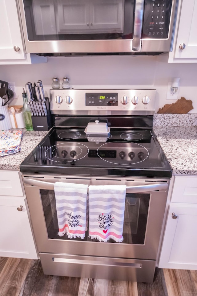 kitchen with appliances with stainless steel finishes, dark wood-type flooring, white cabinets, and light stone counters