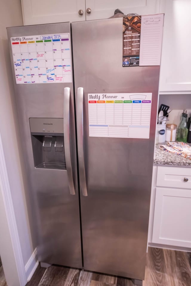 interior details with white cabinetry, dark hardwood / wood-style flooring, light stone counters, and stainless steel fridge