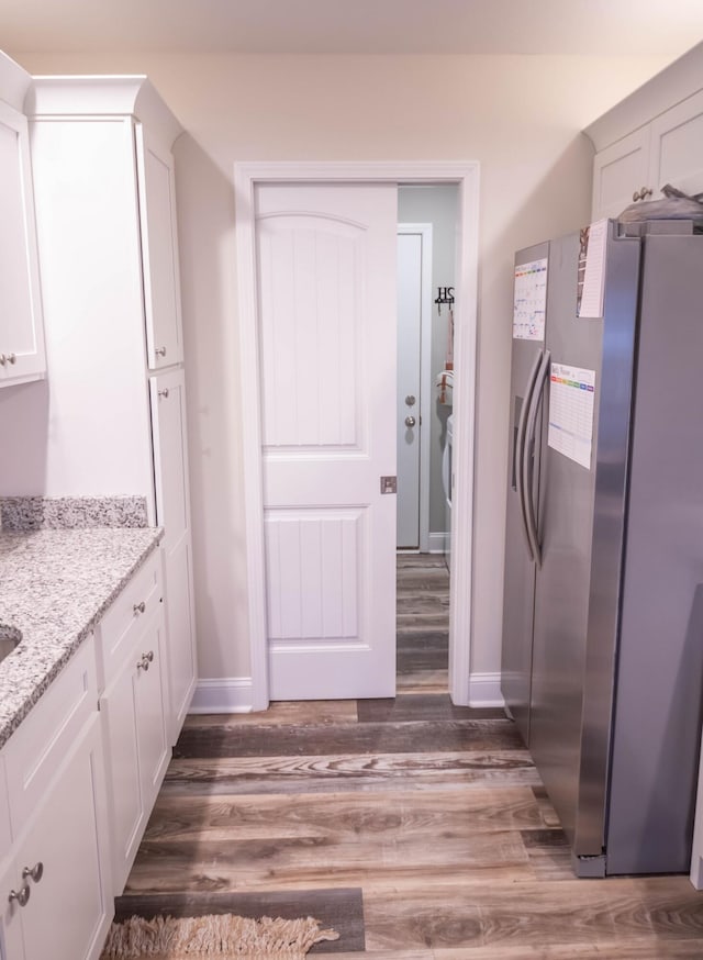 kitchen featuring light stone counters, stainless steel fridge, dark wood-type flooring, and white cabinets