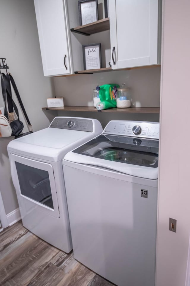 clothes washing area with wood-type flooring, washing machine and dryer, and cabinets