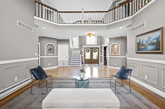 living room featuring a high ceiling, a baseboard heating unit, hardwood / wood-style floors, and french doors