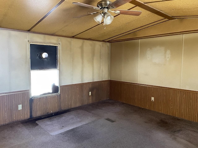 carpeted spare room with ceiling fan, wooden walls, and vaulted ceiling