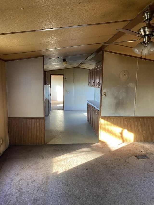 carpeted spare room featuring ceiling fan, lofted ceiling, and wooden walls