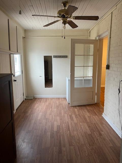 empty room featuring hardwood / wood-style flooring, wood ceiling, brick wall, and ceiling fan