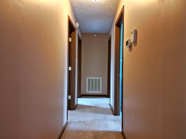 hallway featuring light colored carpet and a textured ceiling