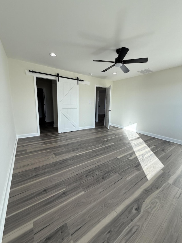 unfurnished bedroom featuring a barn door, dark wood-type flooring, and ceiling fan