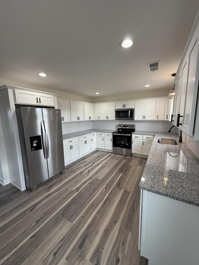 kitchen featuring appliances with stainless steel finishes, white cabinetry, sink, dark stone countertops, and decorative backsplash