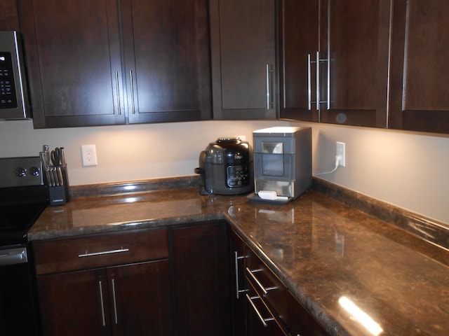 kitchen featuring dark brown cabinetry, dark stone counters, and range with electric stovetop