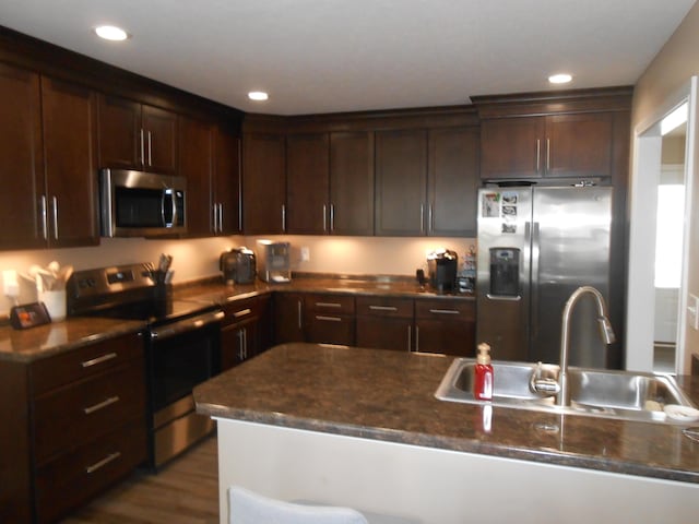 kitchen with stainless steel appliances, sink, dark stone countertops, and dark brown cabinetry