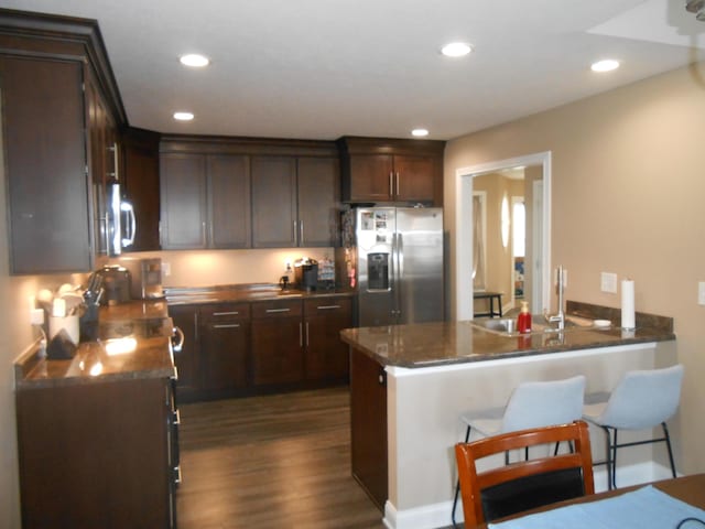 kitchen featuring sink, dark stone countertops, dark hardwood / wood-style flooring, stainless steel appliances, and dark brown cabinets